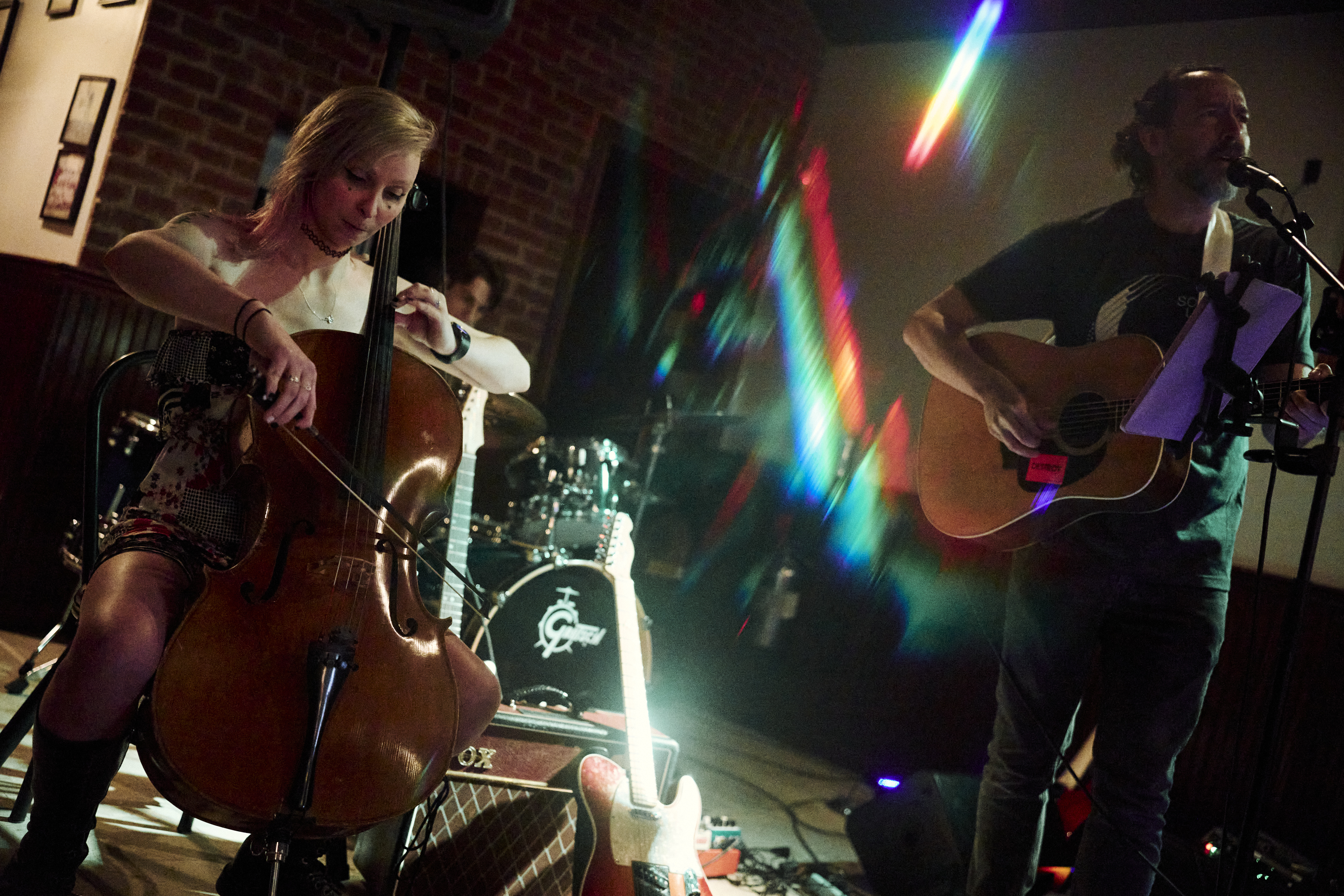 Hailey on cello during Carcasso set at Ormsby Cafe in Pittsburgh. Strange light refraction occurs on glare from polished guitar neck casting ghostly color shifted duplicate images of the guitar across the image
